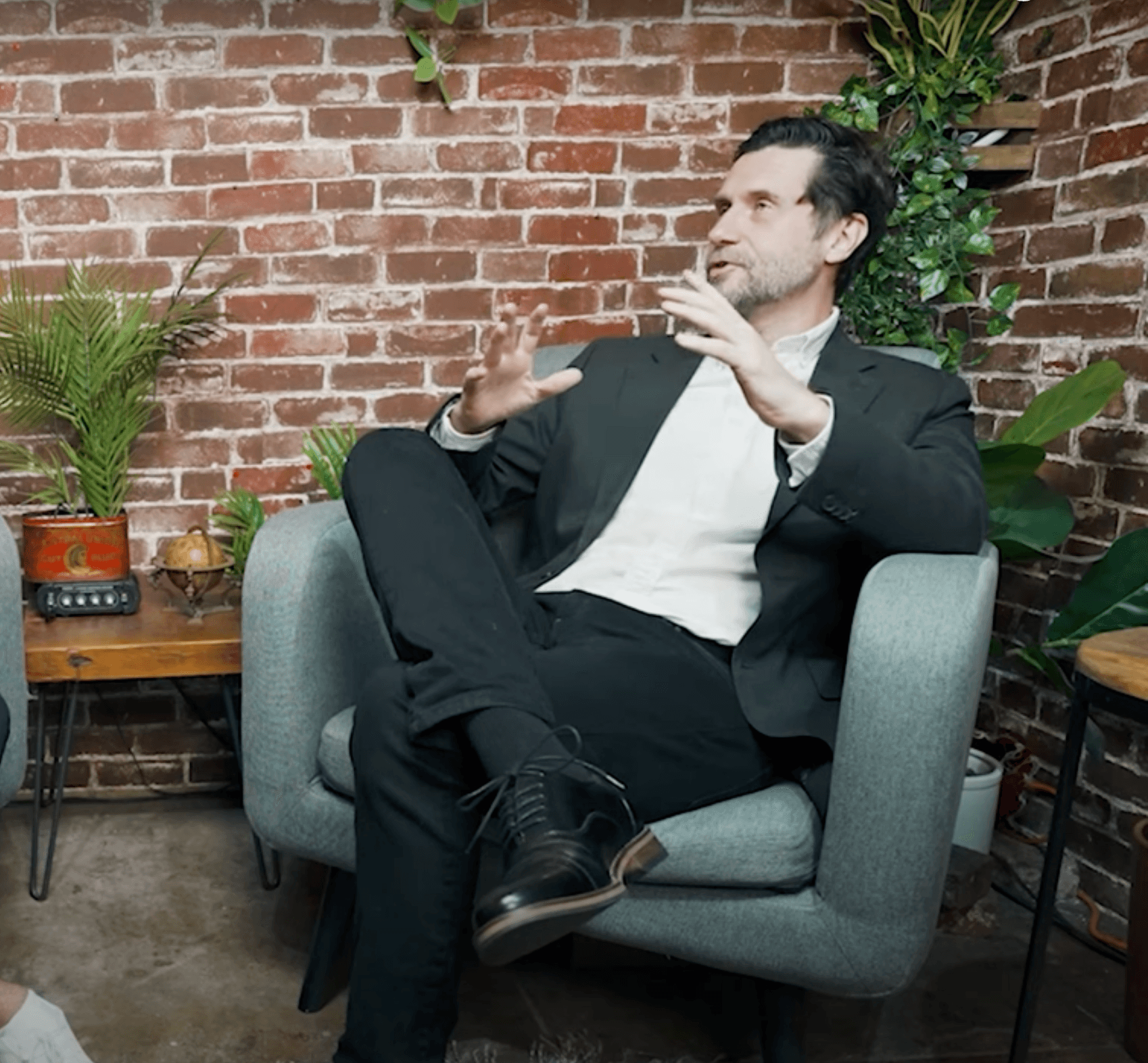 Podcast guest in a suit seated against an exposed-brick studio wall